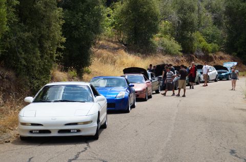 1993 Ford Taurus - Multiple cars are parked on the side of a road during a gathering.