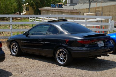 1993 Ford Taurus - A black coupe with a sunroof and aftermarket wheels is parked on a gravel lot.