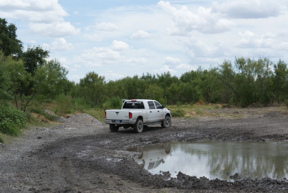 White pickup truck driving on a muddy track near a puddle