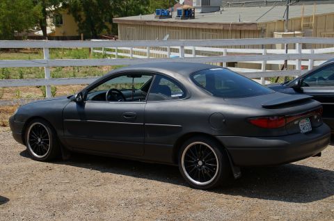 1993 Ford Taurus - This matte black coupe features a spoiler and aftermarket wheels, seen from a three-quarter rear angle.