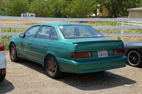1993 Ford Taurus - A green sedan is parked outdoors next to another vehicle, with a white fence in the background.