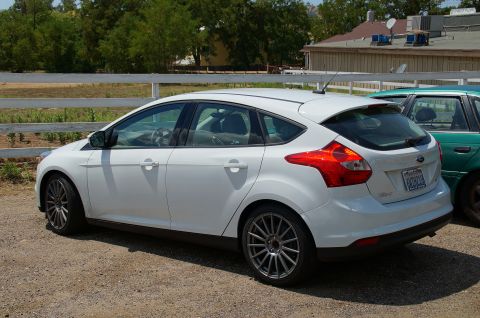 1993 Ford Taurus - A white hatchback is parked outdoors next to a green vehicle.