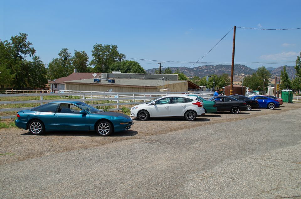 Teal coupe parked on asphalt, side view. Multiple cars in background
