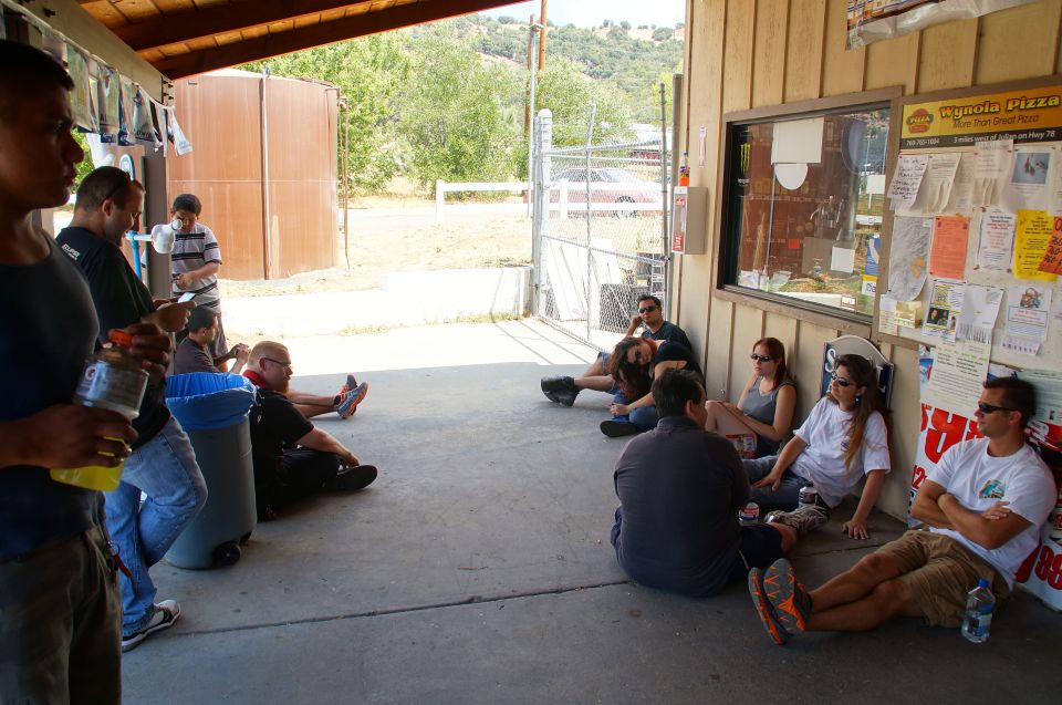 People sitting on a concrete patio outside a building with a window and bulletin board