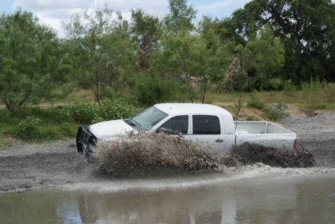 1989 Ford Bronco - White pickup truck navigates through a muddy off-road area.