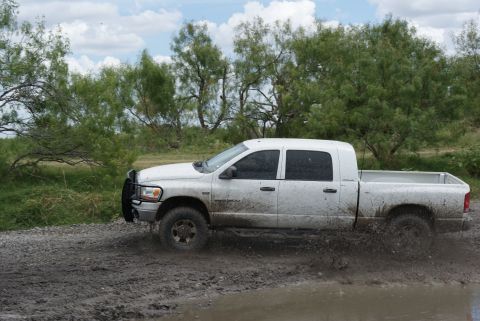 1989 Ford Bronco - A white pickup truck navigates a muddy terrain, kicking up water as it drives.