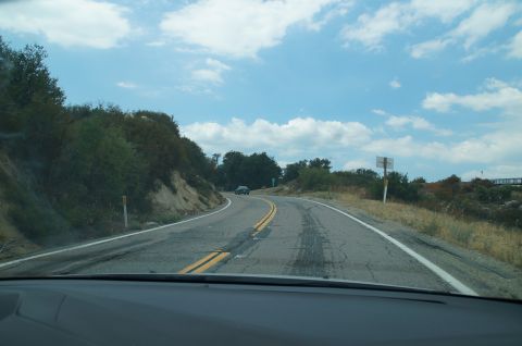 1993 Ford Taurus - A single car travels on a two-lane road through a hilly, vegetated area under a partly cloudy sky.
