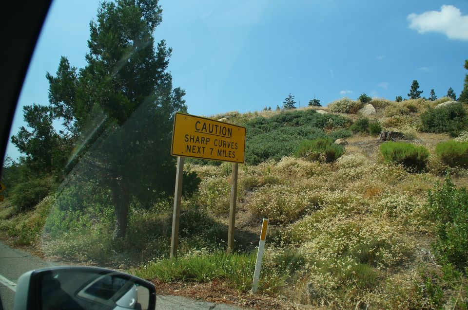 Yellow caution sign with text 'CAUTION SHARP CURVES NEXT 7 MILES' on a hillside