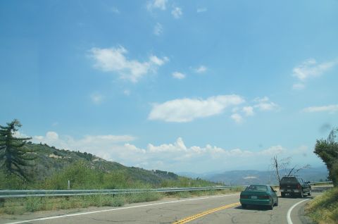 1993 Ford Taurus - Two vehicles travel along a winding road under a bright, cloudy sky with distant hills.