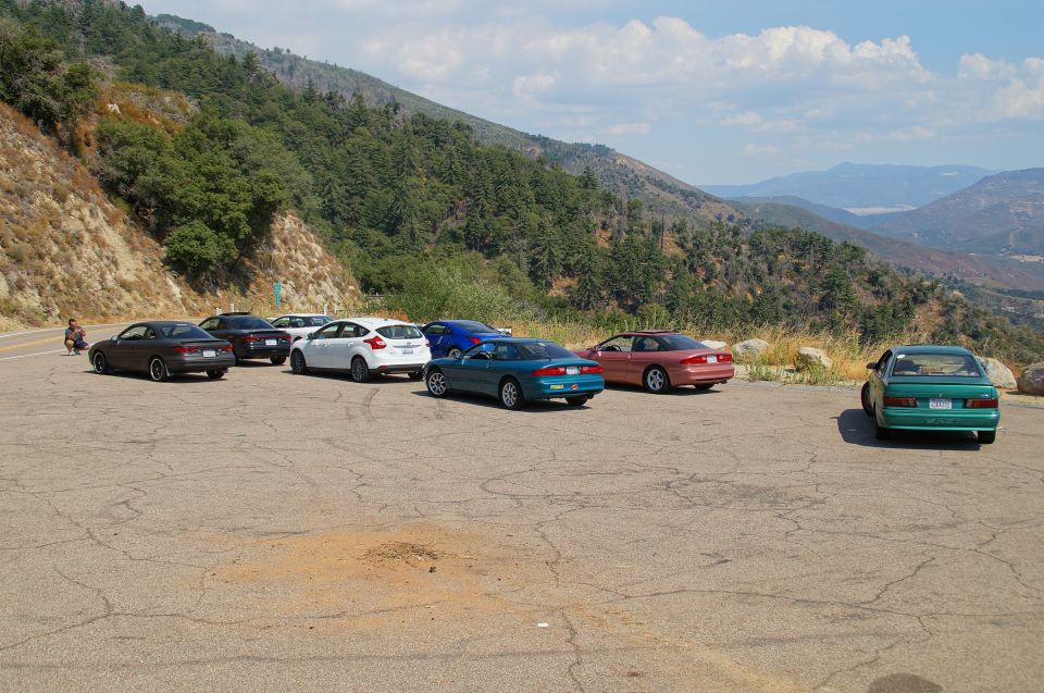 Several cars parked in a lot on a mountainside with a valley in the background