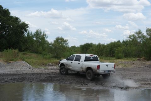 1989 Ford Bronco - A white pickup truck navigates a muddy off-road course, sending up a spray of dirt.
