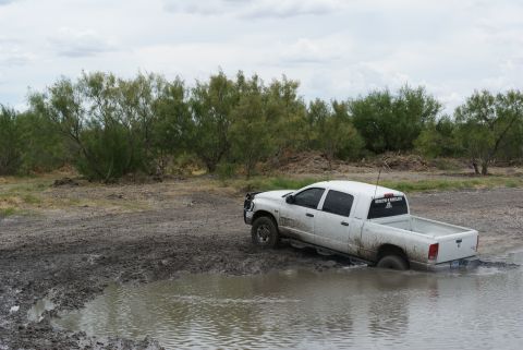 1989 Ford Bronco - White pickup truck stuck in mud with trees and overcast sky in the background.
