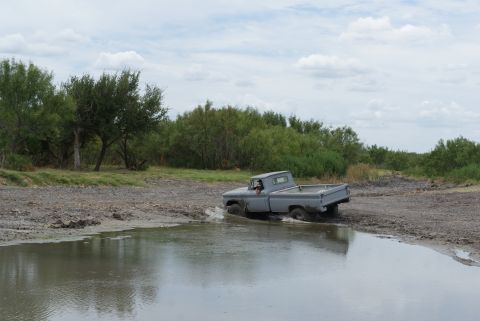 1989 Ford Bronco - A vintage pickup truck navigates through a muddy off-road area under a cloudy sky.
