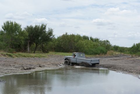 1989 Ford Bronco - A gray pickup truck navigates through a muddy, watery terrain with dense foliage in the background.