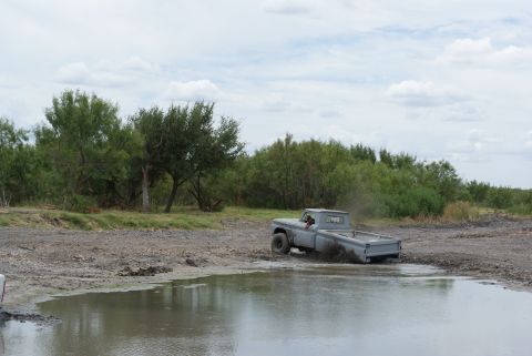 1989 Ford Bronco - An old pickup truck navigates a muddy off-road course under a cloudy sky.