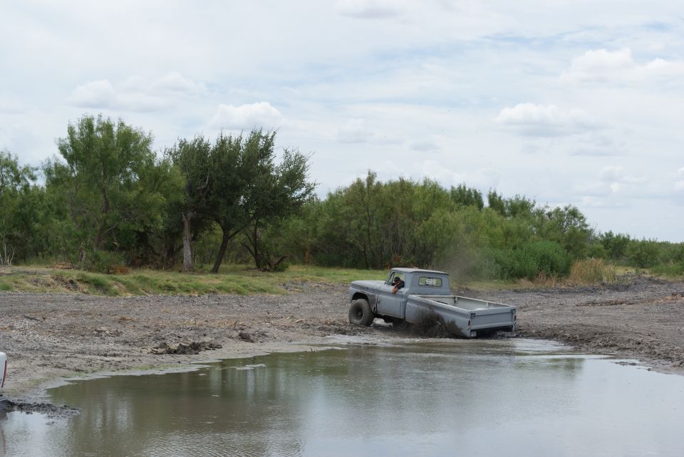 Gray pickup truck driving through a muddy puddle with trees in the background