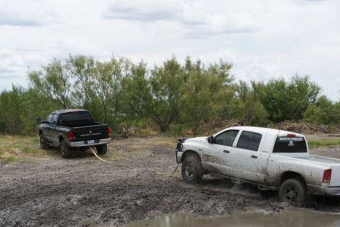 1989 Ford Bronco - Two trucks are stuck in the mud, with one attempting to tow the other out.