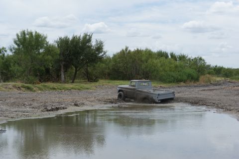 1989 Ford Bronco - A gray pickup truck is stuck in a mud puddle with trees and brush in the background.