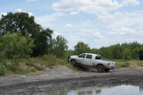 1989 Ford Bronco - A white pickup truck navigates a muddy, off-road terrain under a cloudy sky.