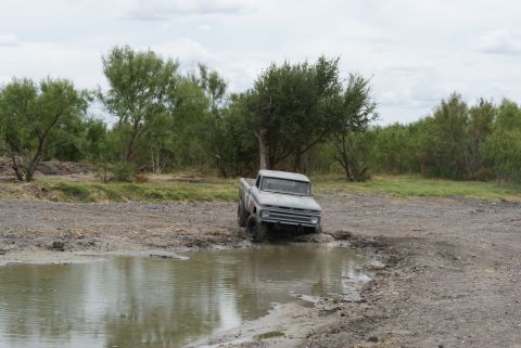 1989 Ford Bronco - A vintage pickup truck navigates a muddy obstacle course in a rural setting.