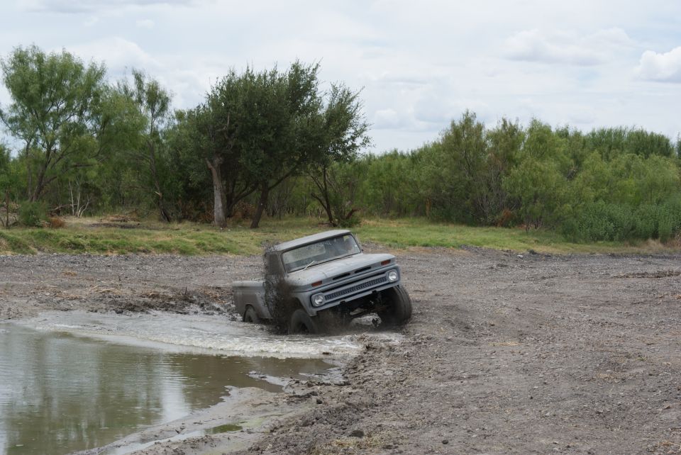 Gray pickup truck stuck in a muddy puddle, front end angled up