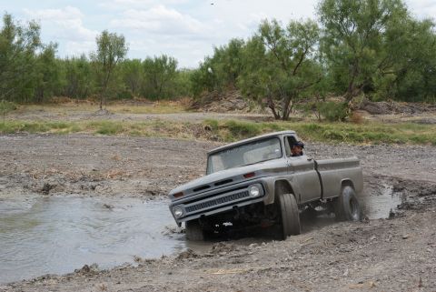 1989 Ford Bronco - This vintage pickup truck navigates a challenging muddy terrain with water splashing.
