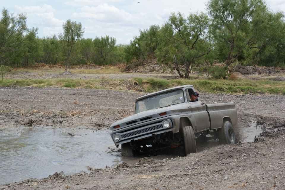 Gray pickup truck driving through a muddy puddle. Driver visible