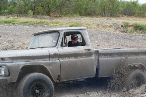 1989 Ford Bronco - A driver navigates a muddy off-road course in a classic pickup truck, kicking up water as much water as dirt.