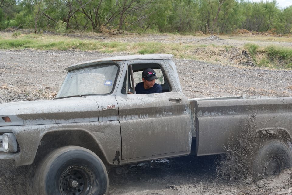 Mud-covered 1960s pickup truck splashing through water