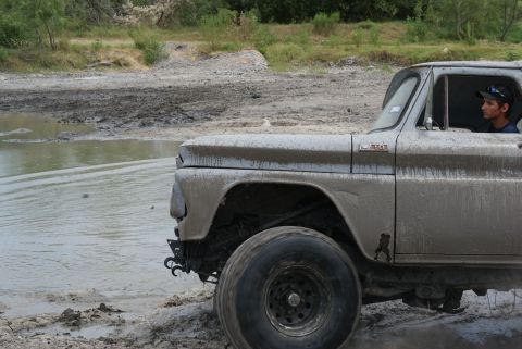 1989 Ford Bronco - Vintage pickup truck navigates through muddy water, tires partially submerged.