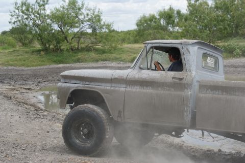1989 Ford Bronco - A driver navigates a muddy off-road course in a heavily soiled pickup truck.