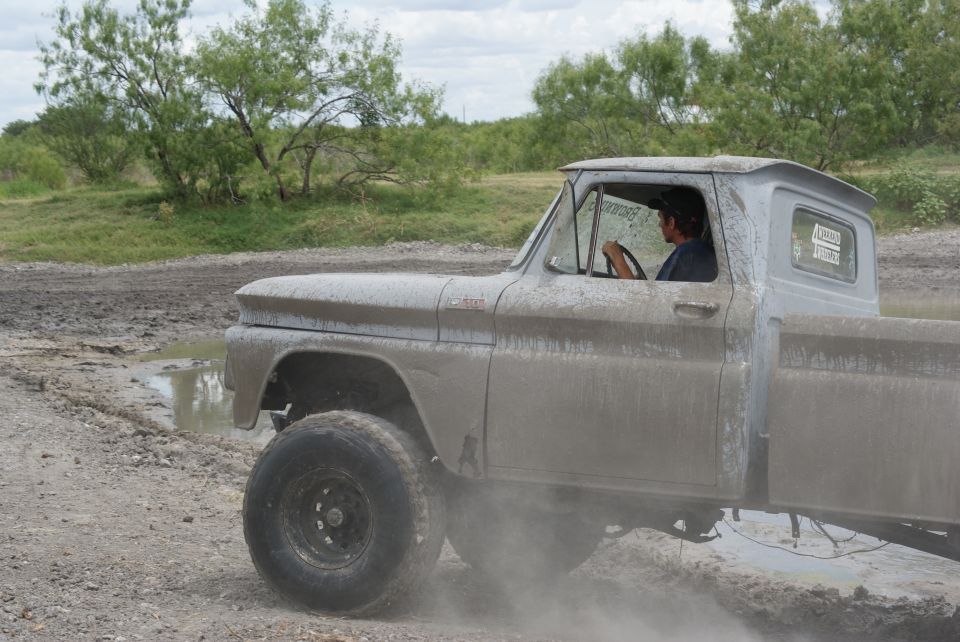Muddy pickup truck driving through a dirt and mud track with a person driving