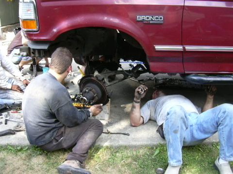 1991 Ford Bronco - Mechanics are performing maintenance on the front axle and brake assembly of a red Ford Bronco.