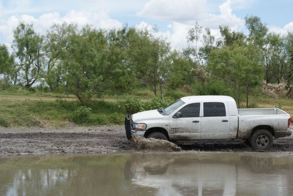 White pickup truck with four doors stuck in mud and water, trees in background