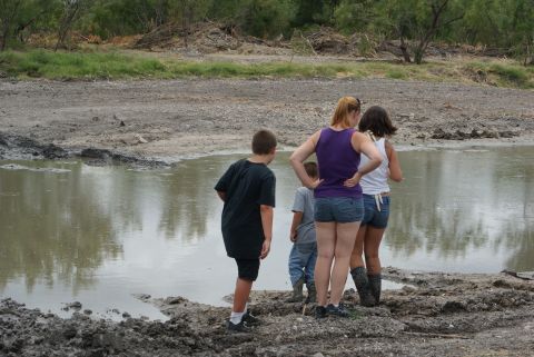 1989 Ford Bronco - A group of people observe a muddy area with water and debris, suggesting an outdoor recreational scene.