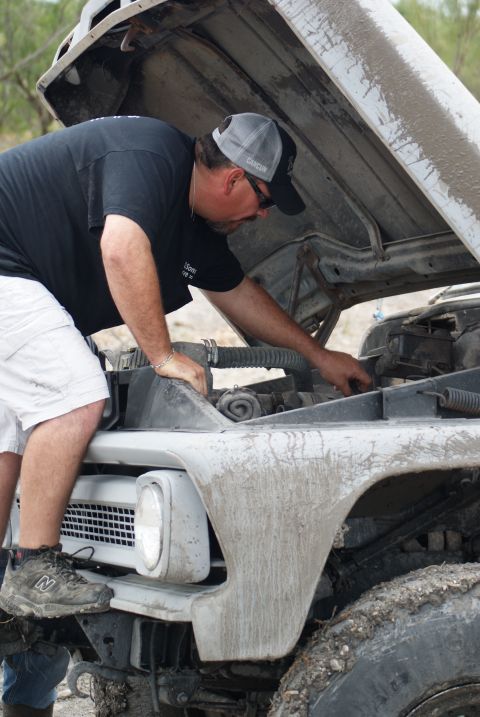 1989 Ford Bronco - A man inspects the engine of a mud-covered vehicle with the hood open.