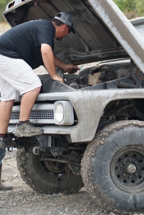 1989 Ford Bronco - A man works on the engine of a mud-covered 1970s Ford truck.