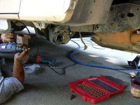 1991 Ford Bronco - Mechanic works on the suspension of a vehicle, drilling into a component.