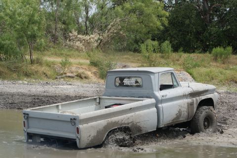 1989 Ford Bronco - A light gray pickup truck is stuck in the mud, with its rear end submerged.