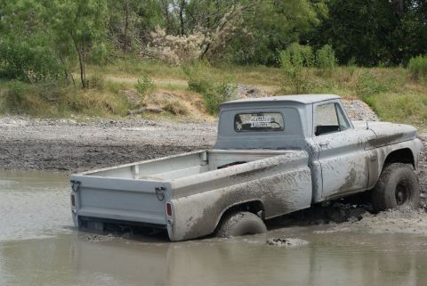 1989 Ford Bronco - A classic gray pickup truck is stuck deep in the mud, with only its front wheels and cab visible above the murky water.