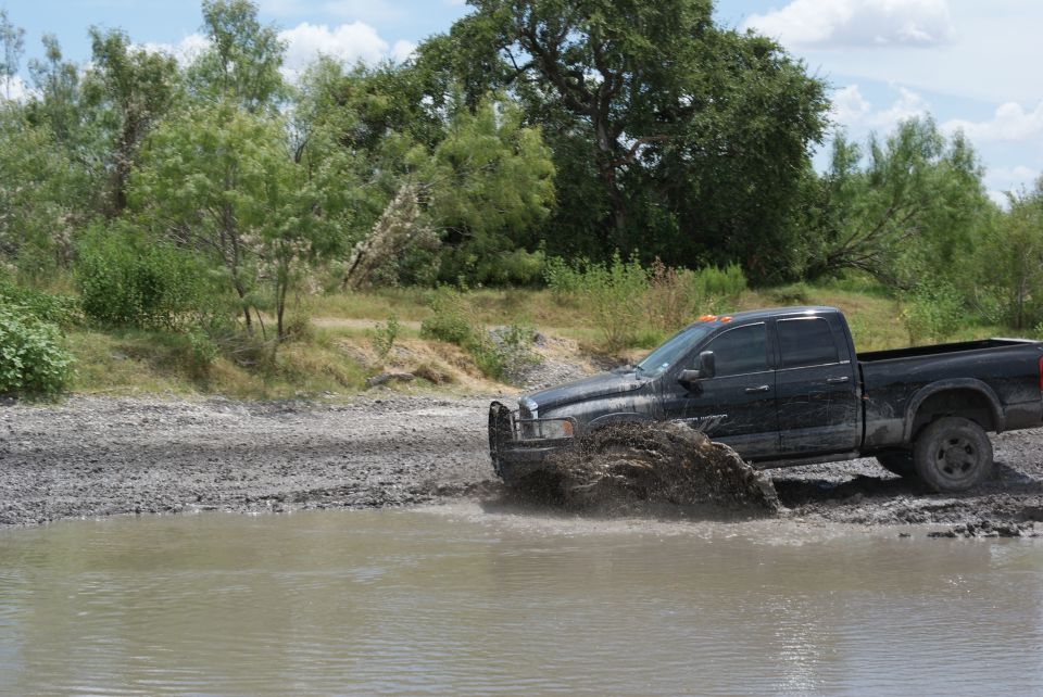Black pickup truck splashing mud while driving through shallow water and mud