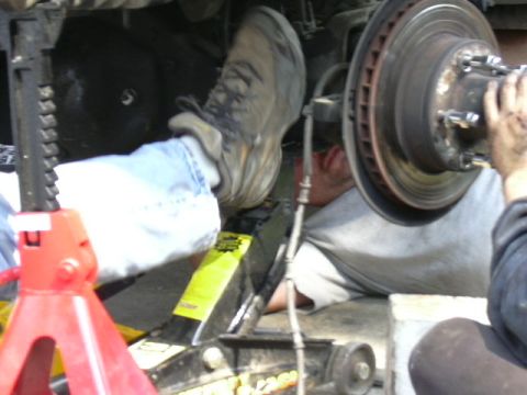 1991 Ford Bronco - A mechanic works on the suspension of a vehicle, supported by jack stands and a floor jack.