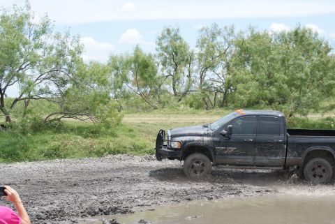 1989 Ford Bronco - A black pickup truck navigates through a muddy terrain under a cloudy sky.