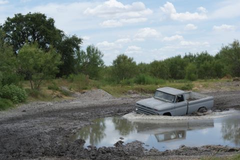 1989 Ford Bronco - A gray pickup truck is stuck in a mud puddle with water splashing around it.
