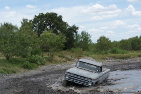 1989 Ford Bronco - This classic pickup truck is navigating a muddy terrain with water splashing around it.
