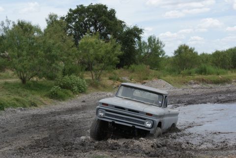 1989 Ford Bronco - A vintage gray pickup truck navigates a muddy terrain, its front end partially submerged.