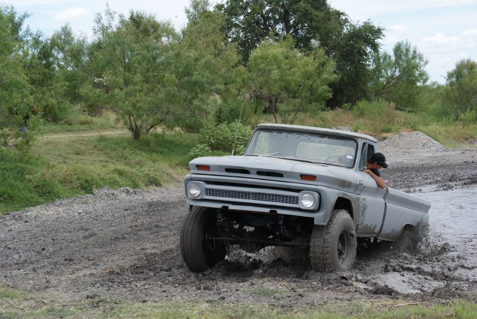 Gray pickup truck with large tires driving through a muddy track