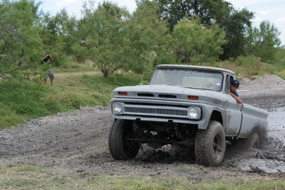 Gray pickup truck driving through mud. Someone is taking a photo in the background