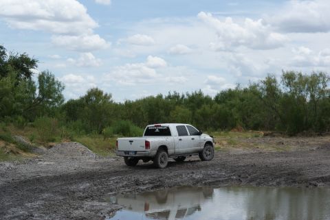 1989 Ford Bronco - White pickup truck navigates a muddy track under a cloudy sky.