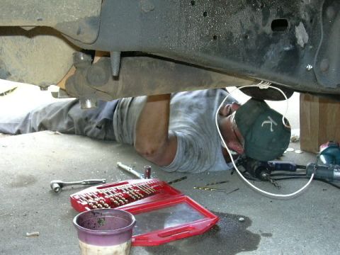1991 Ford Bronco - A person lies on the ground performing maintenance on the undercarriage of a vehicle, surrounded by tools and equipment.